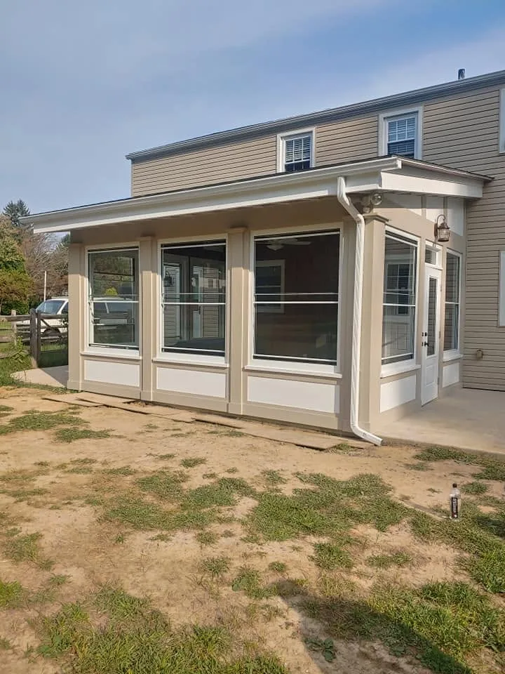 Enclosed porch addition on a two-storey colonial, tan siding with white trim and full-height glazing