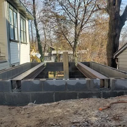 Concrete block foundation with steel beams set, alongside an existing white clapboard house