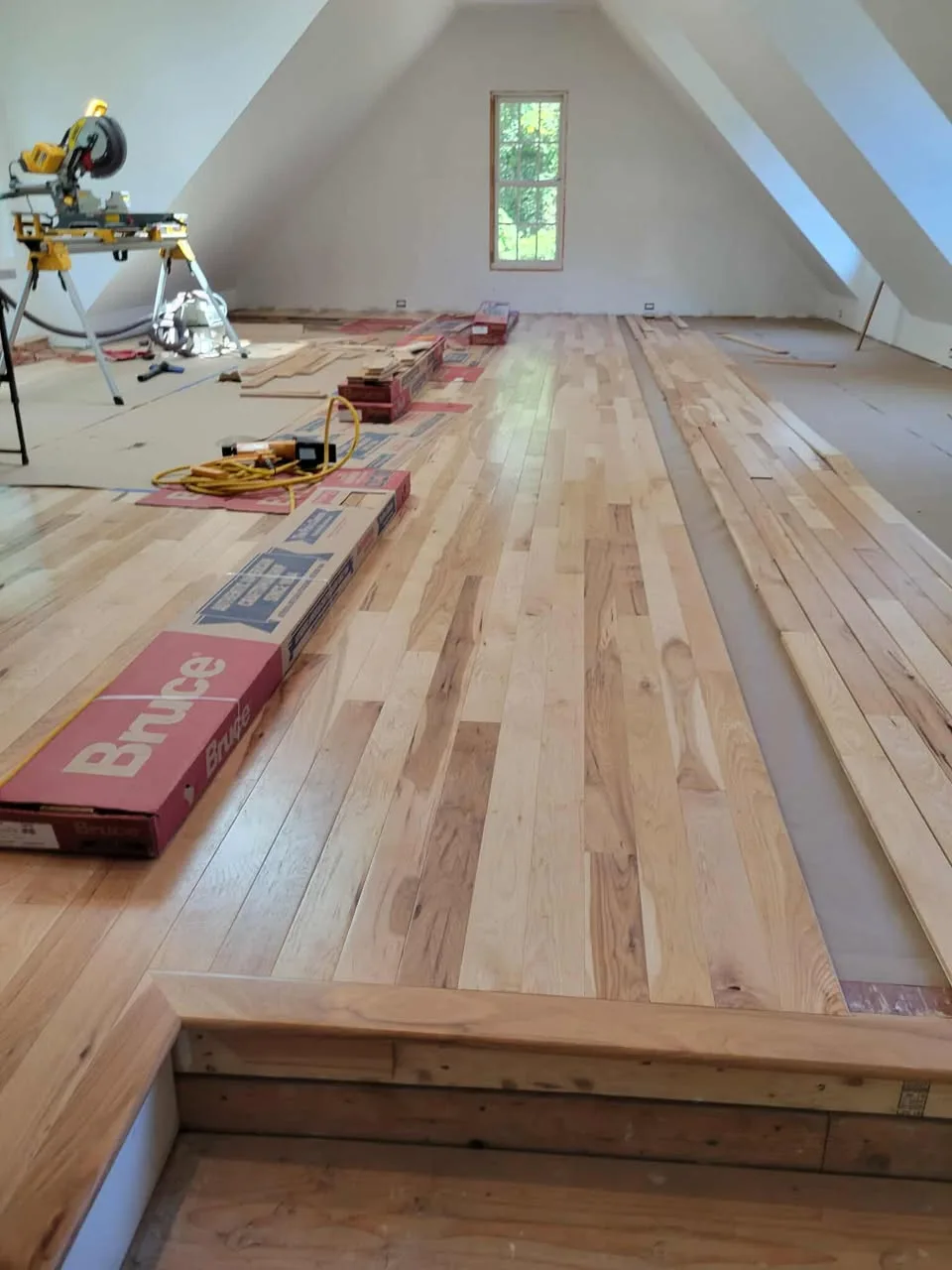Attic room with sloped plastered ceilings and hickory flooring part-laid toward a gable window