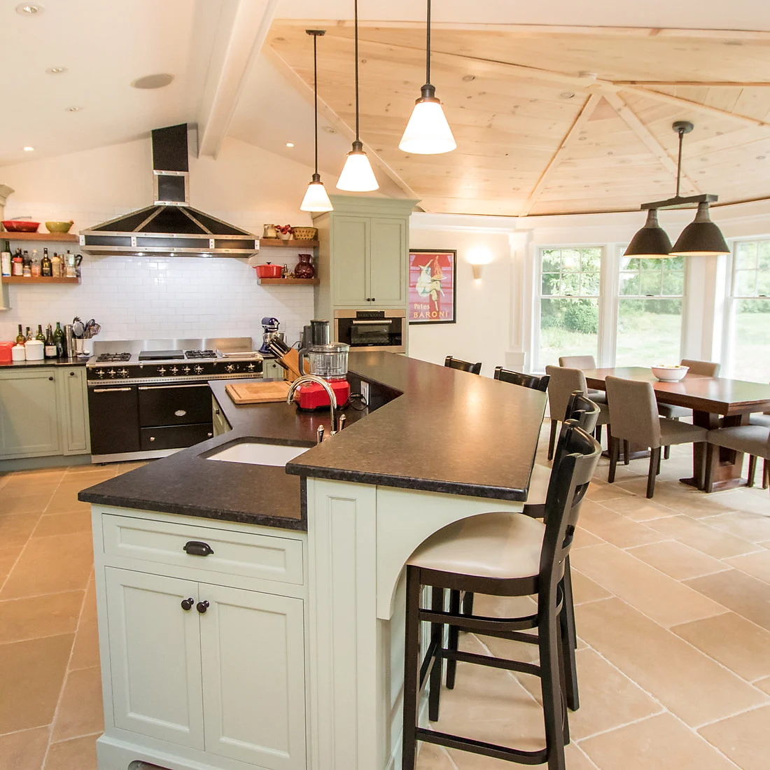 Finished kitchen with sage green island, vaulted pine ceiling, black range and dining table beyond