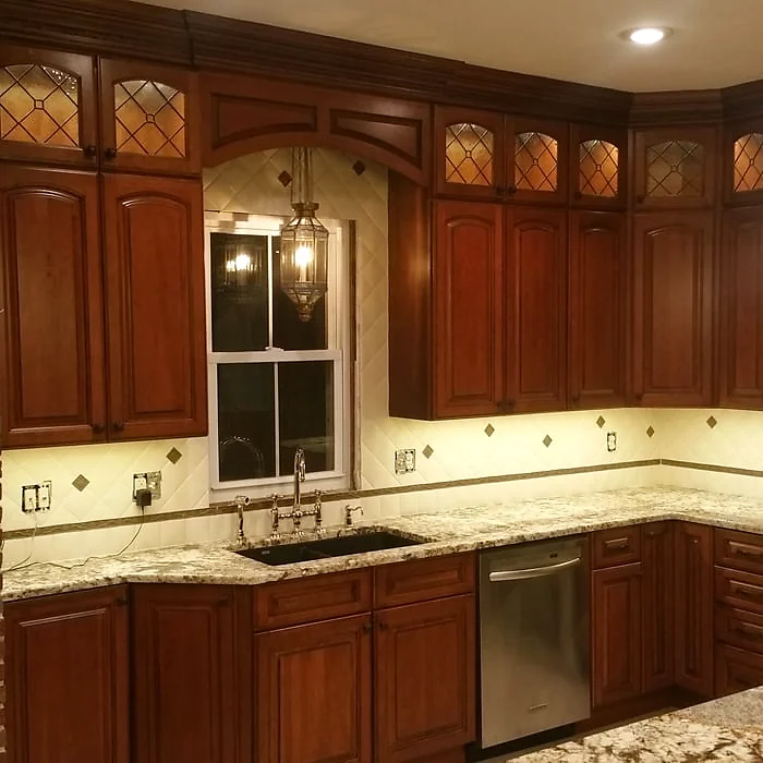 Traditional cherry kitchen with leaded glass upper cabinets, granite counters and a bridge faucet over a dark sink